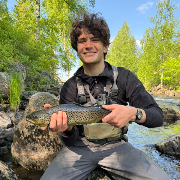 Man holding a fish by a river with trees in the background