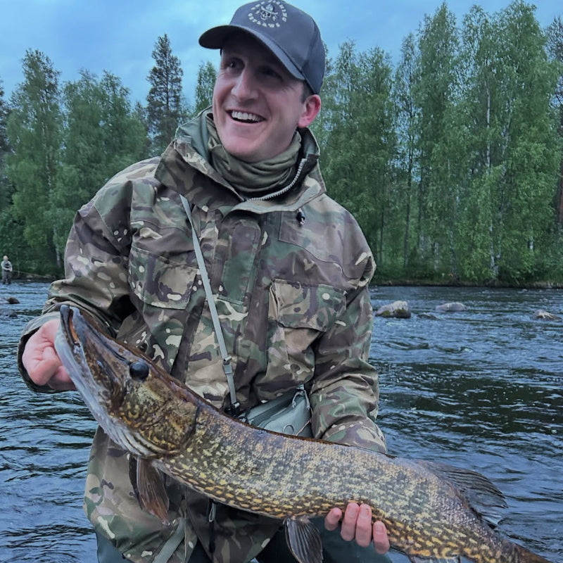 Man holding a large pike in a river with trees in the background