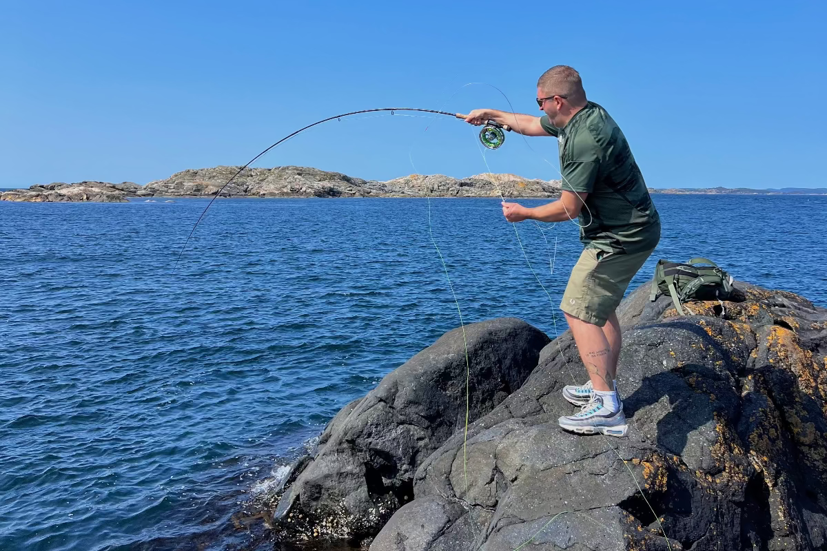 Man fishing on rocks by the water with a clear blue sky