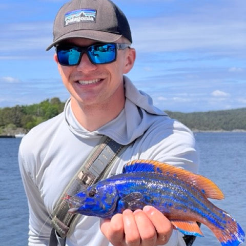 Man holding a cuckoo wrasse by the sea
