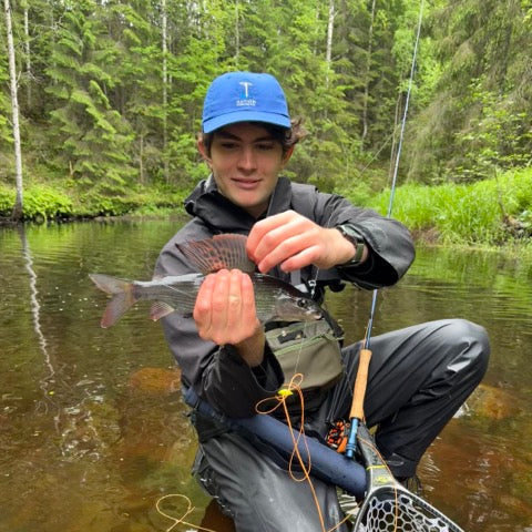 Man holding a fish by a forest stream