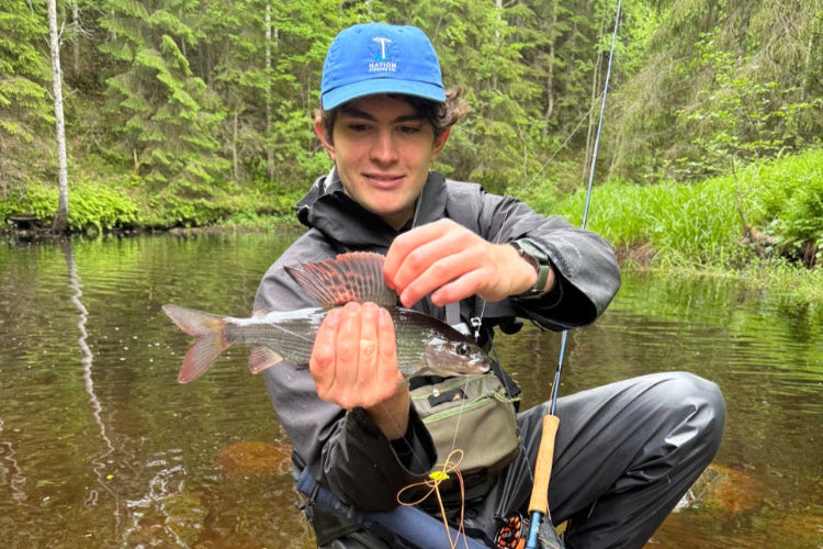 person holding a grayling while fly fishing in a forested area in Finland