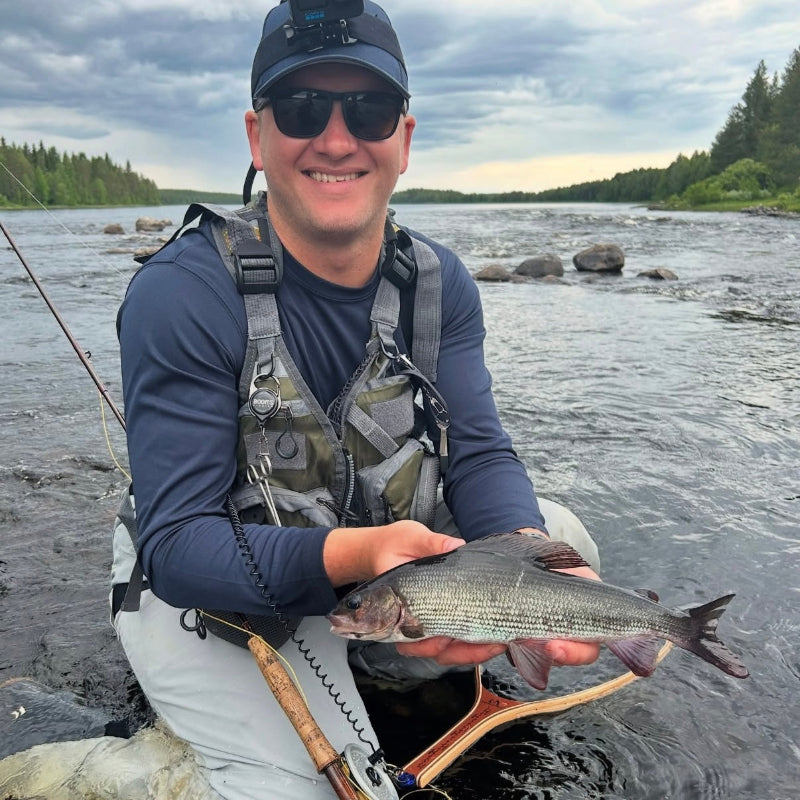Man holding a grayling by a river with fly fishing gear