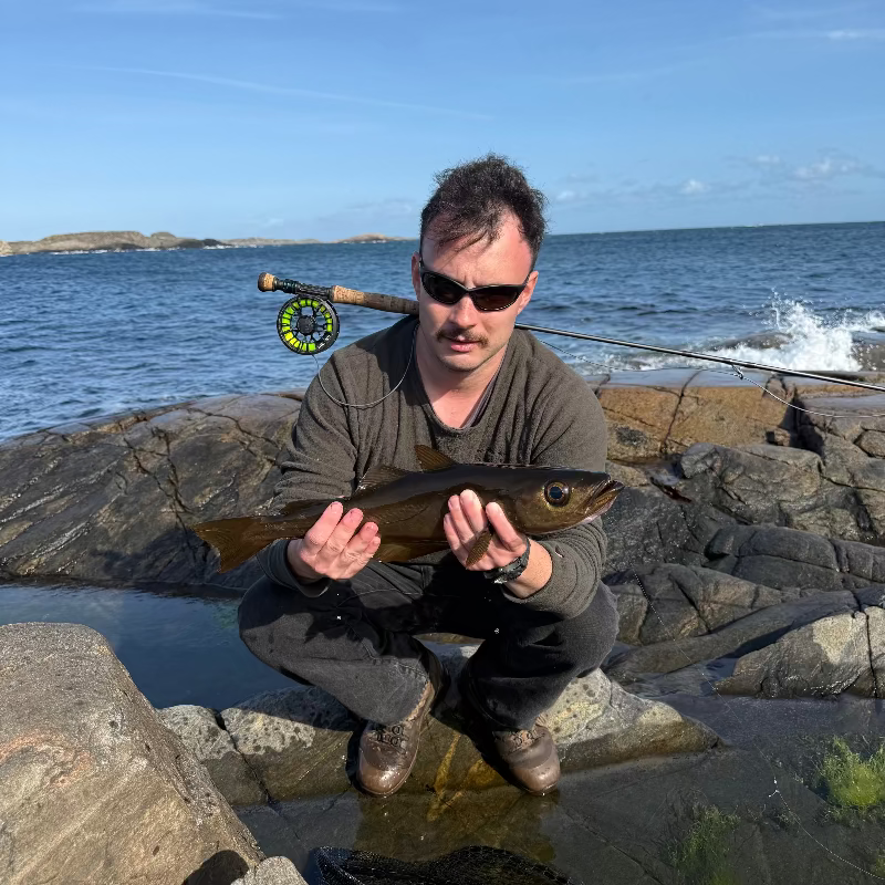 Man holding a fish by the sea with fly fishing equipment on rocks