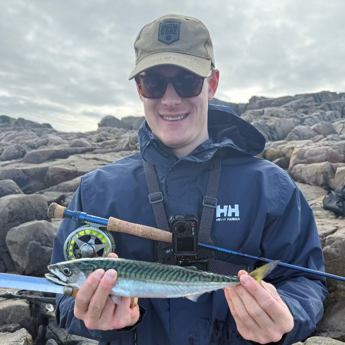Man holding a fish and a fishing rod on rocky terrain