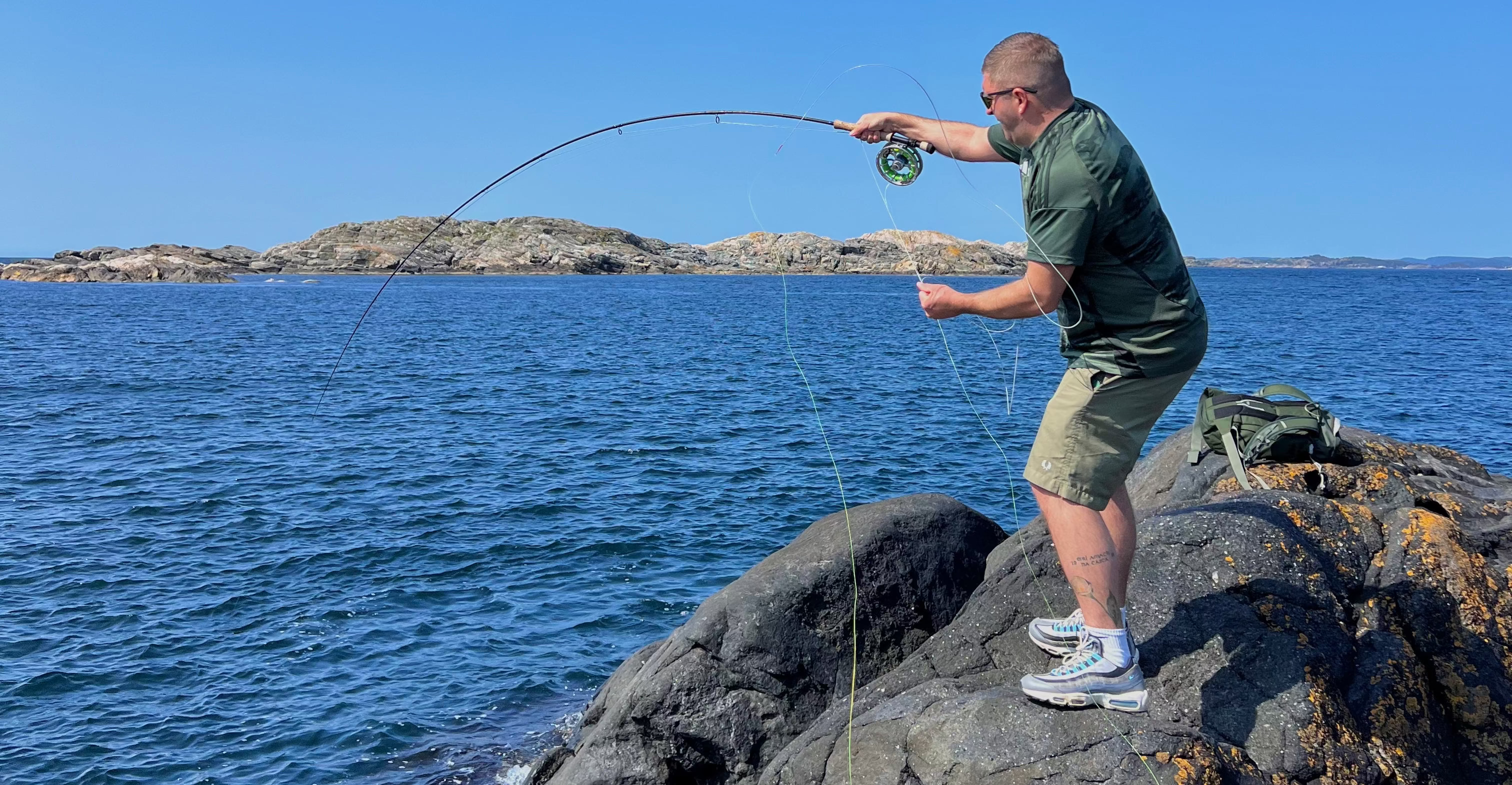 Man fishing on rocks by the sea with clear blue sky
