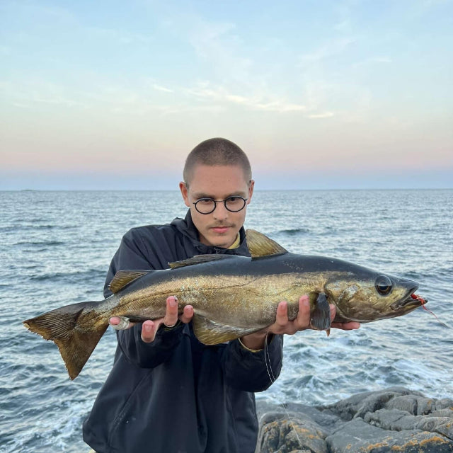 A person holding a large fish with the ocean in the background, indicating a successful fishing trip.