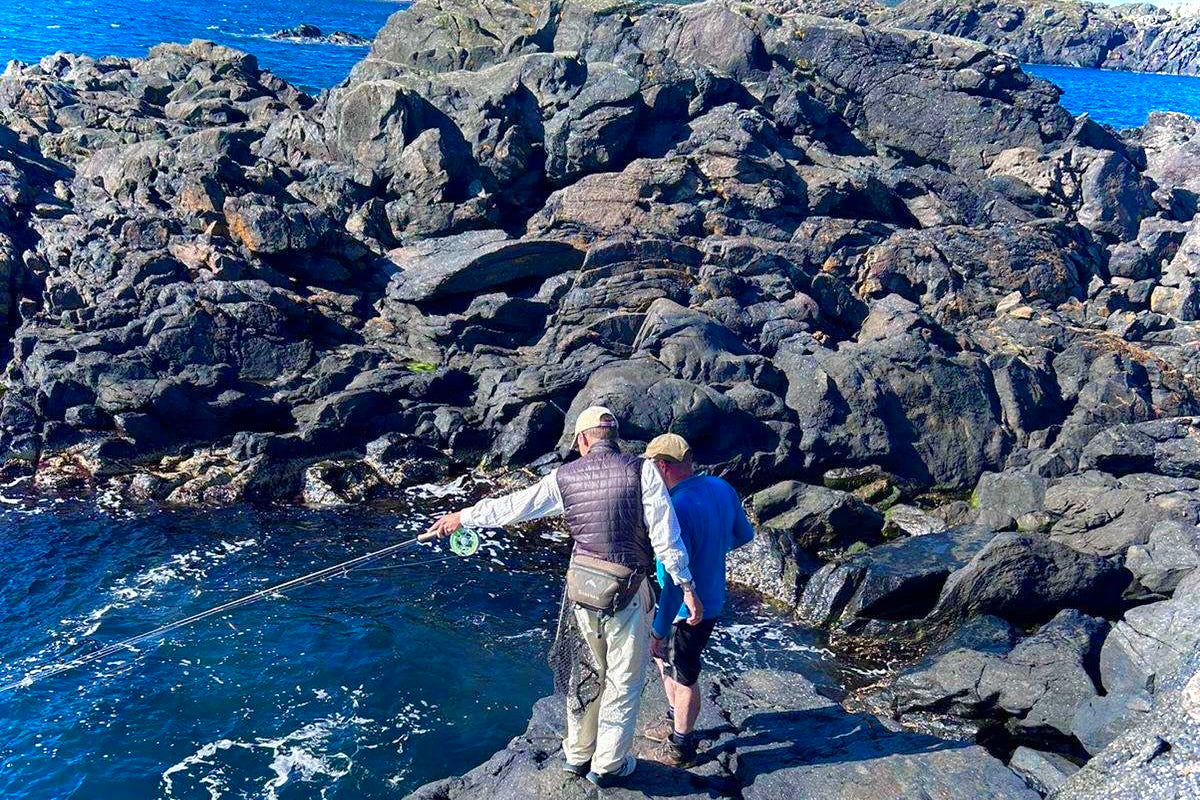 Two people fishing on rocky cliffs by the ocean.