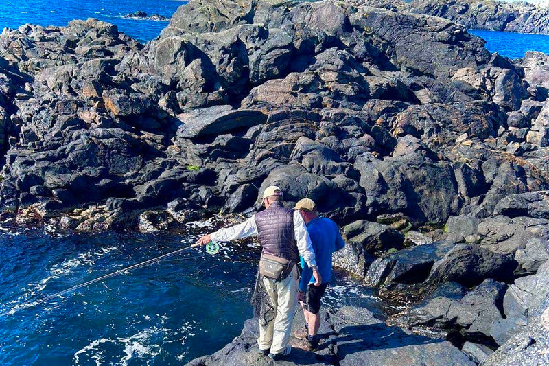 Two people fishing on rocky cliffs by the ocean.