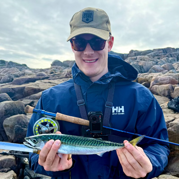 Man holding a fish and a fishing rod on rocky terrain