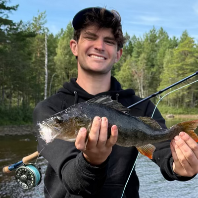 Man holding a fish caught while fishing by a lake with trees in the background